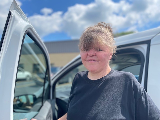 Emma stands outside an agency van on a sunny day, smiling.