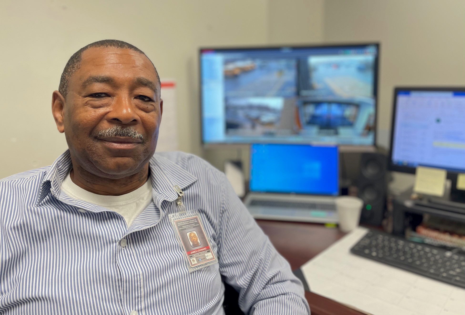 Smiling man sitting in office with computer screens behind him.