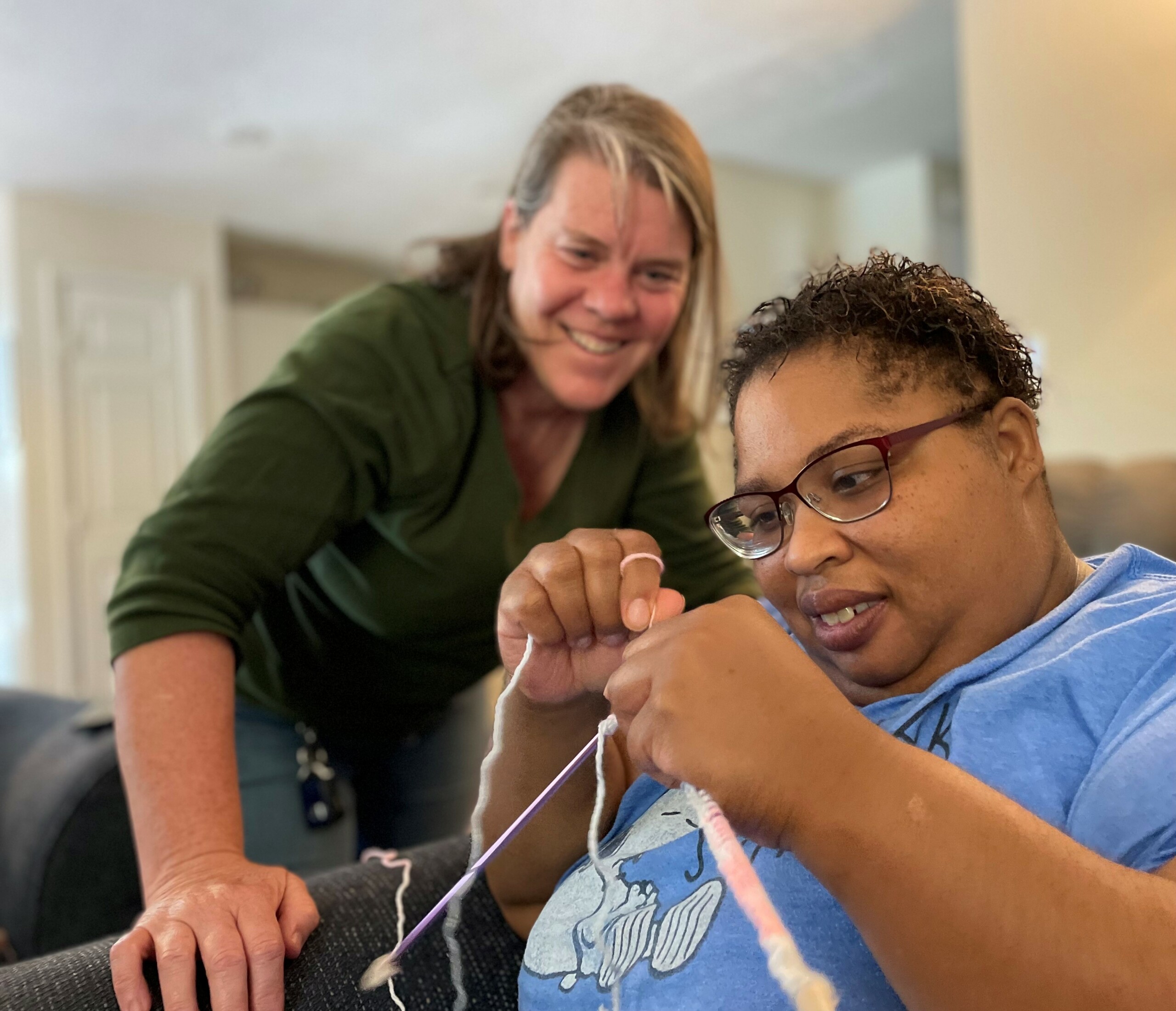 Knitting teacher watches her adult student knitting with pink yarn.