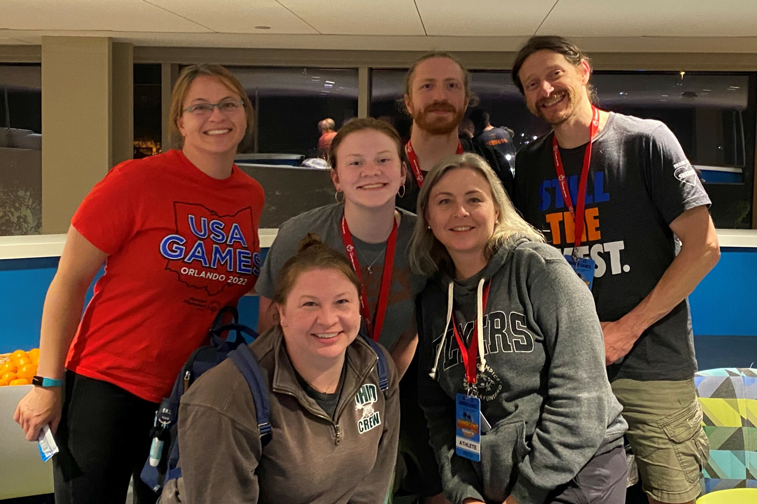 Three women, one teen girl and two men who are all family gather together, smiling.