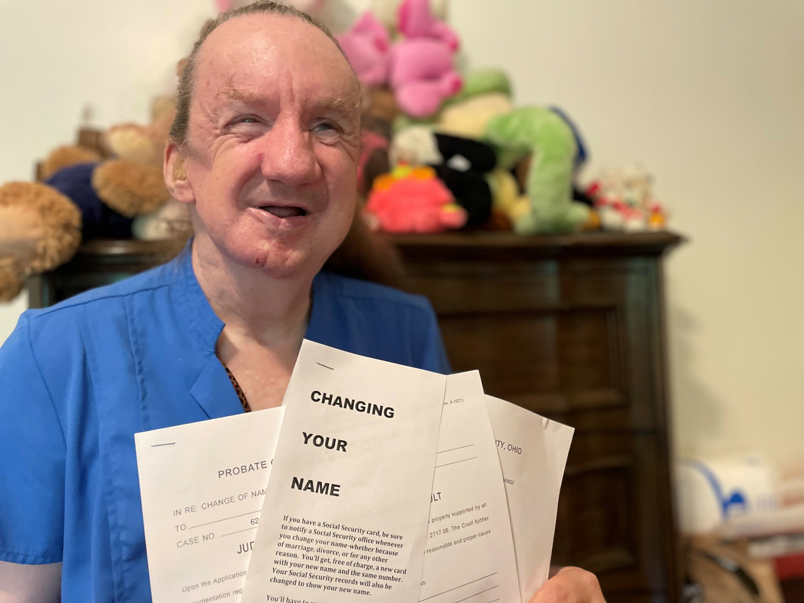 Smiling woman in bright blue shirt, holding court documents for changing her name.