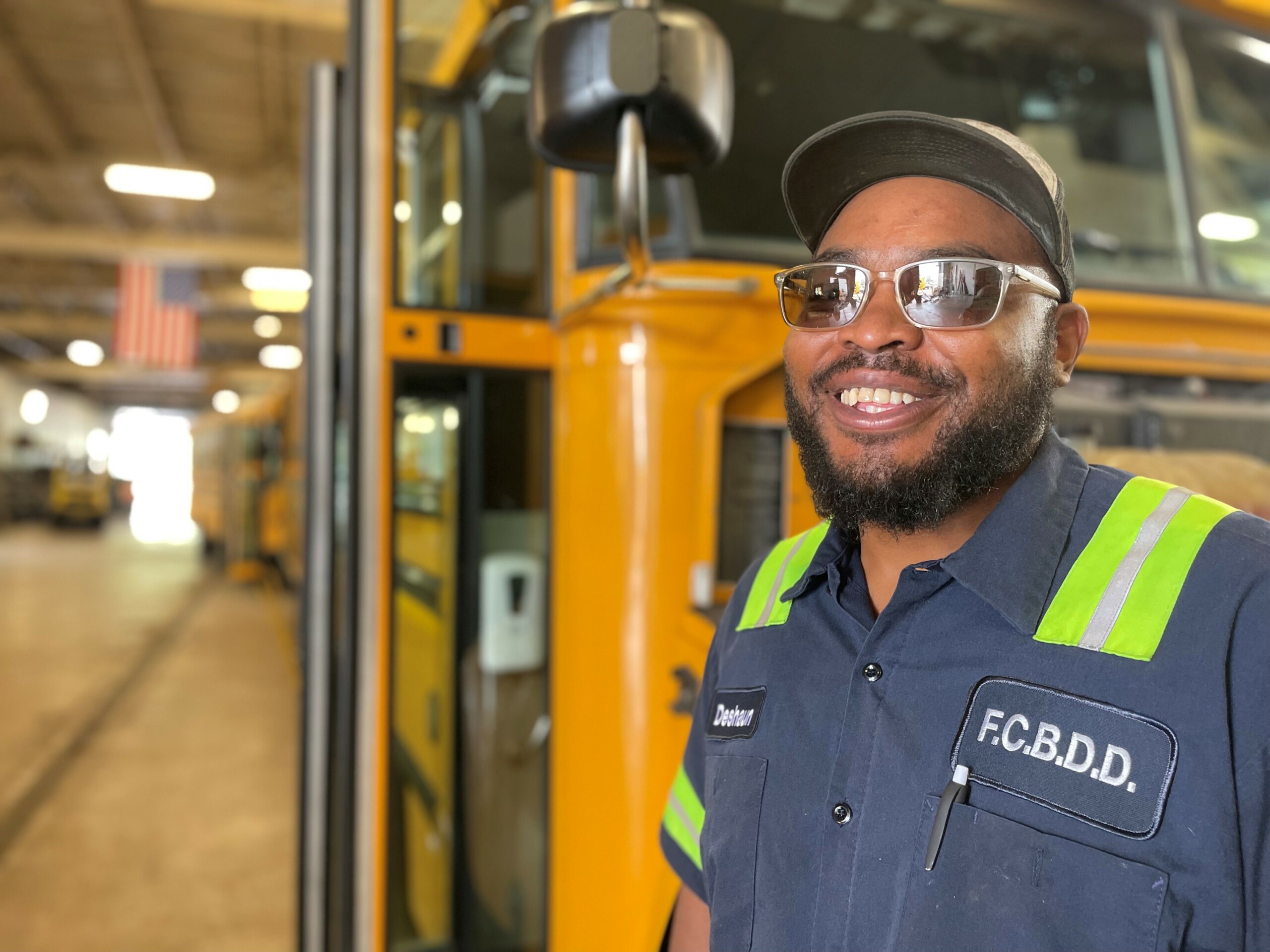 Man wearing sunglasses smiling and standing in front of a school bus.