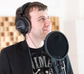 Man wearing headphones standing in front of a microphone.